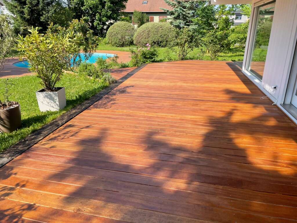 Terrasse en lames de bois le long d’une maison, avec jardin et piscine